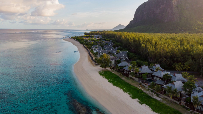 Longue plage de sable blanc et petit village au pied d'une montagne de l'Île Maurice
