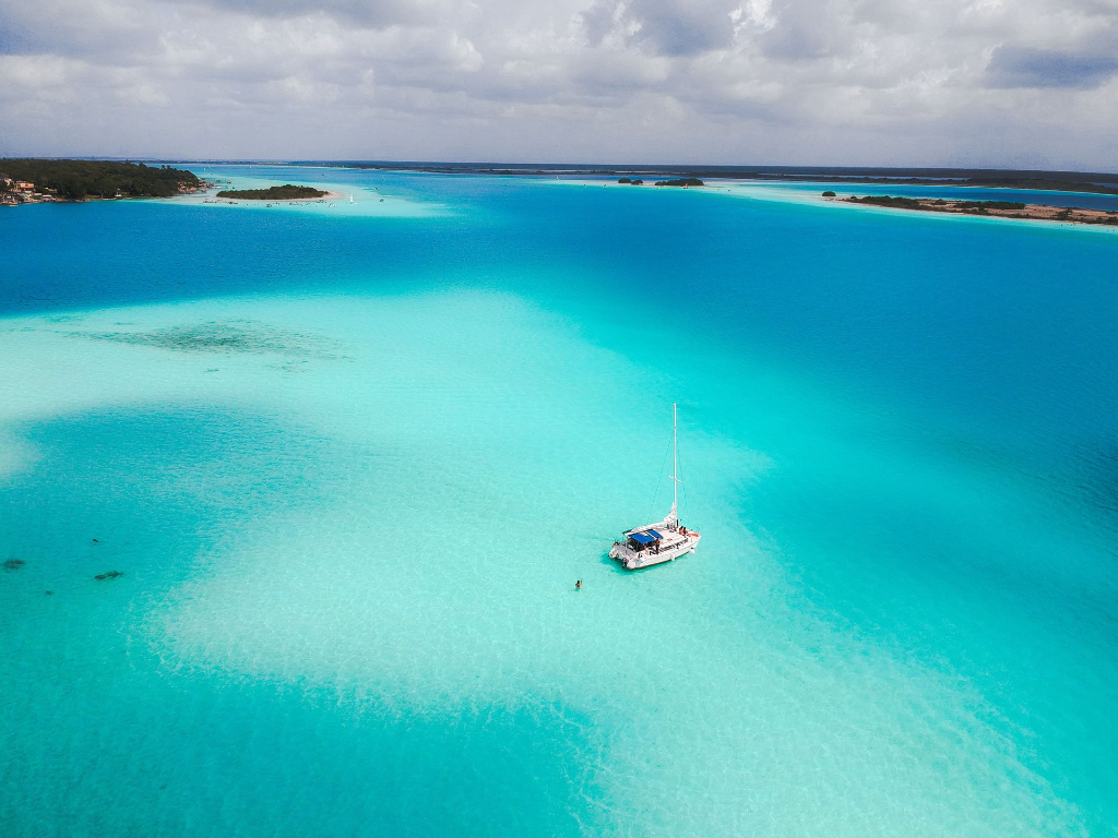 Une vue aérienne époustouflante d'un voilier dans les eaux turquoise tranquilles de la lagune de Bacalar, au Mexique.