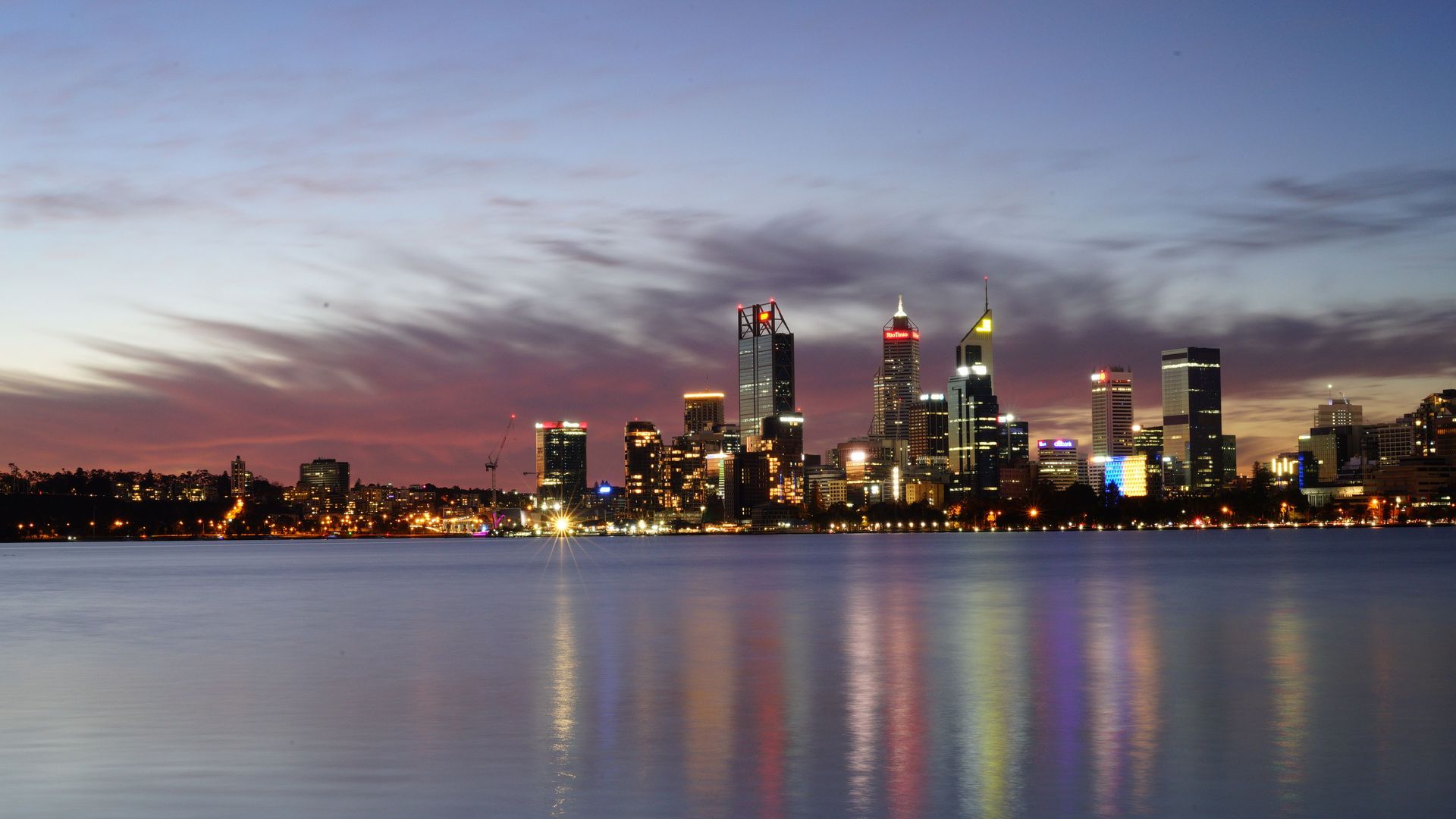 Une vue à couper le souffle de la skyline illuminée de Perth se reflétant sur l'eau calme au crépuscule.