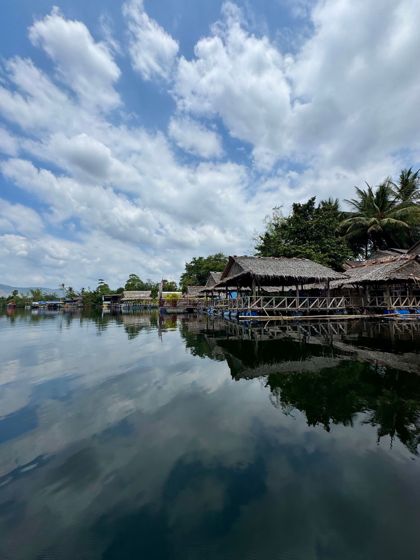 Charmantes huttes au bord de la rivière avec des reflets clairs à Kampot, au Cambodge, sous un ciel vibrant.