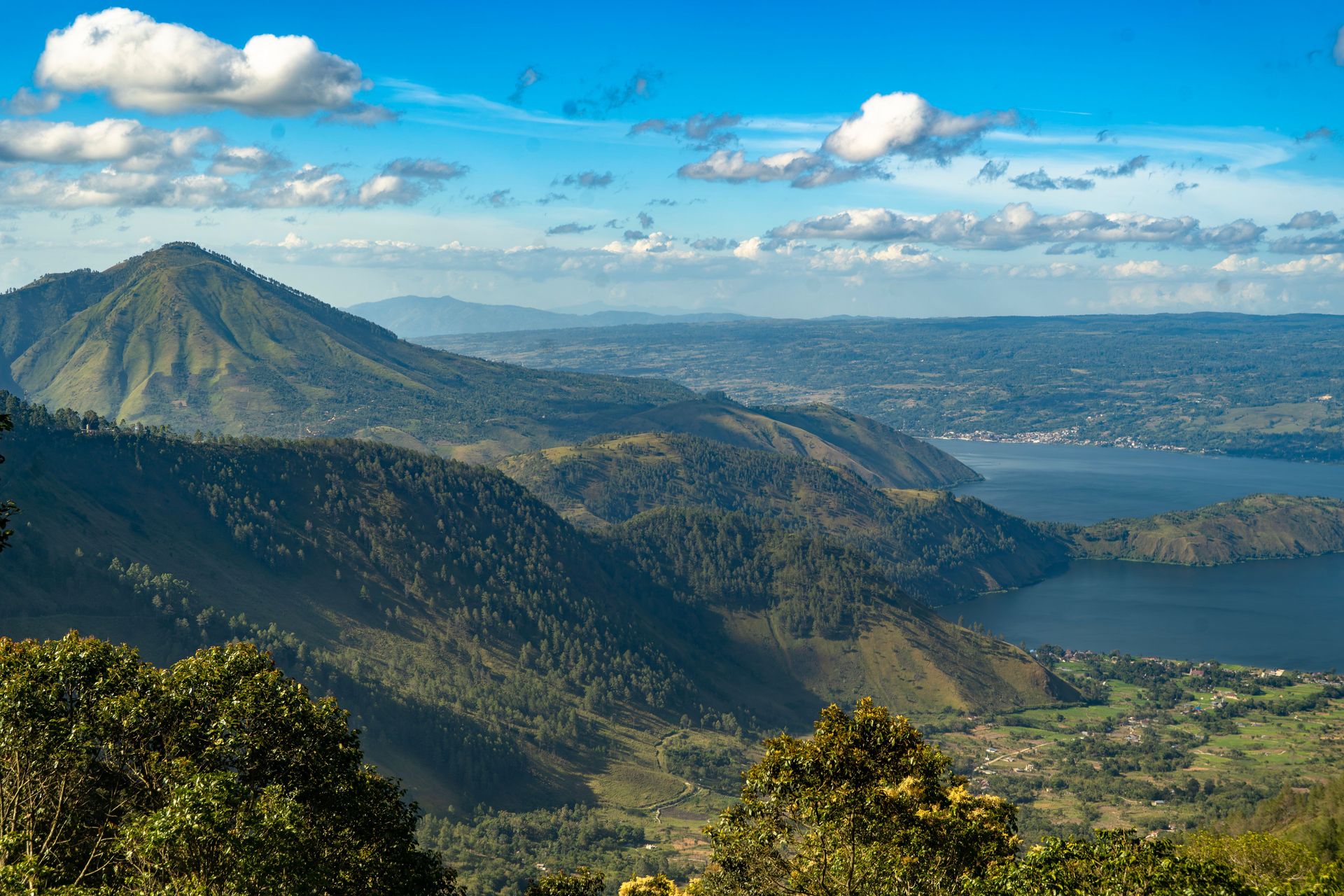 Une vue aérienne à couper le souffle du lac Toba à Sumatra, entouré de paysages montagneux luxuriants sous un ciel éclatant.