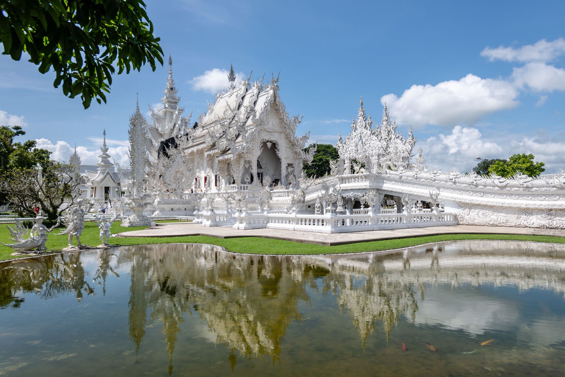 Stunning architecture blanche de Wat Rong Khun reflétée dans un étang tranquille sous un ciel bleu à Chiang Rai, Thaïlande.