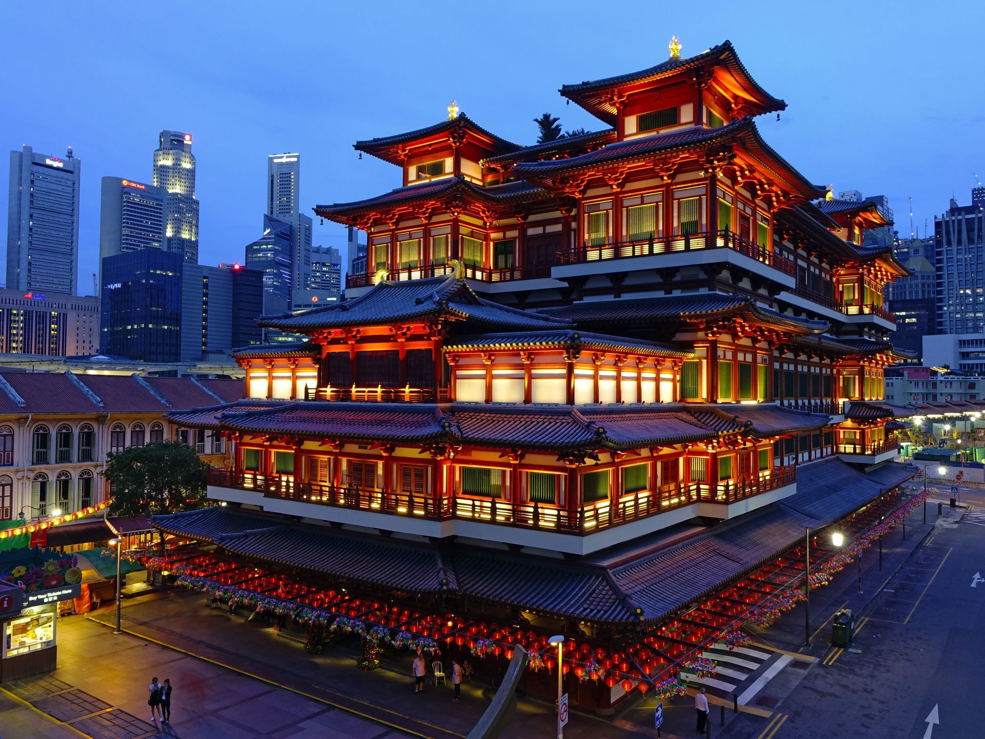 Temple de la relique dentaire de Bouddha illuminé dans le Chinatown de Singapour, avec la skyline de la ville en arrière-plan.