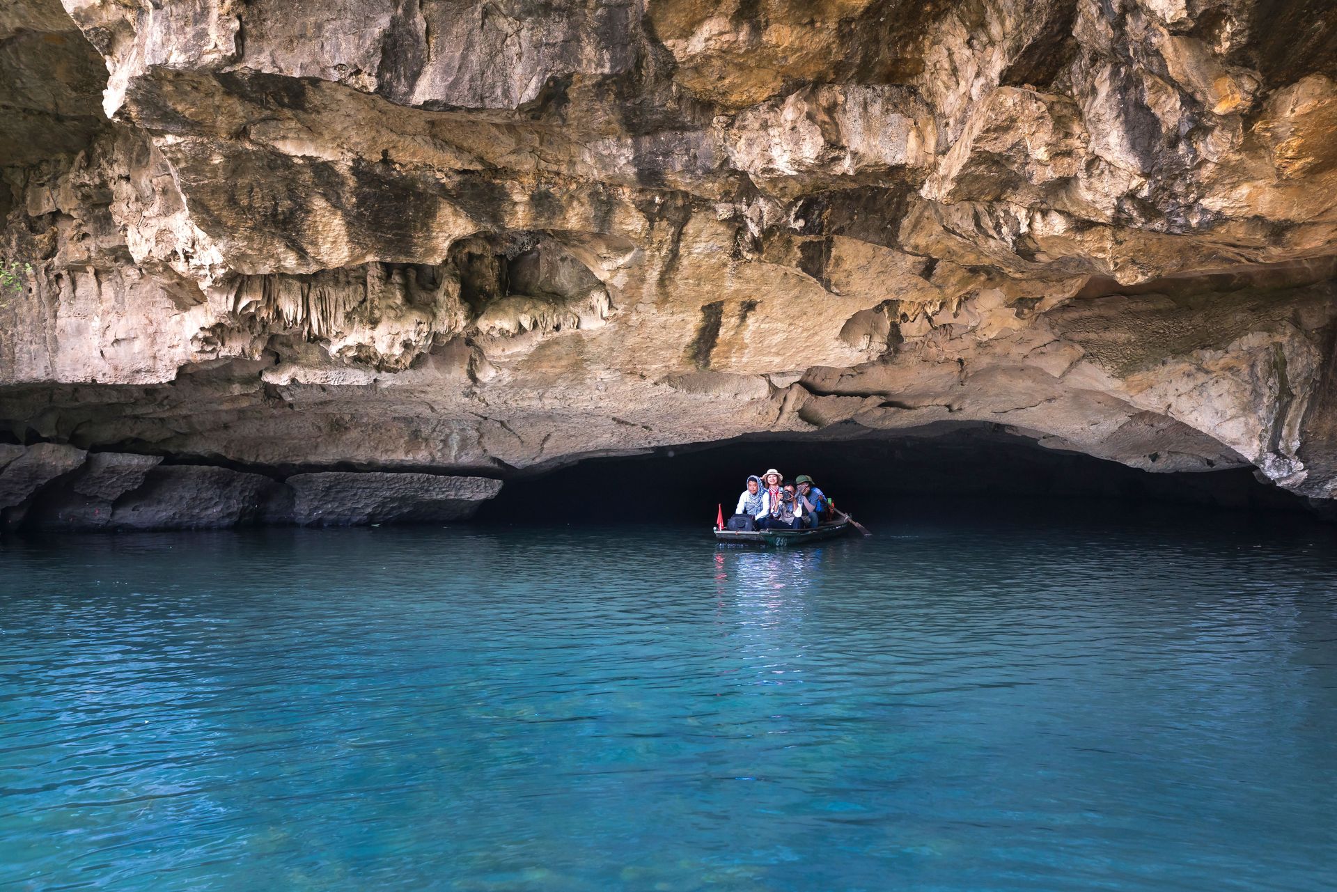 Un groupe de personnes sur un bateau explorant une grotte de calcaire pittoresque avec des eaux bleu clair.