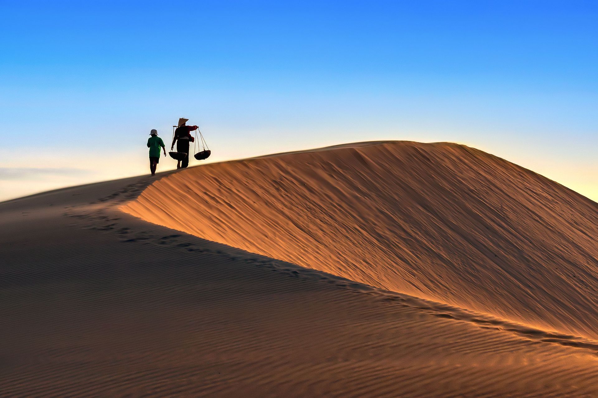 Deux personnes marchent sur les dunes de sable du désert de Mui Ne, au Vietnam, au coucher du soleil.