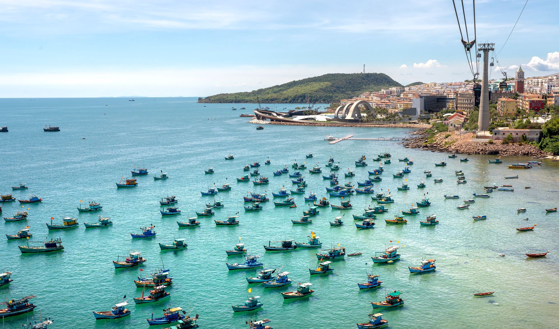 Vue aérienne de bateaux de pêche colorés sur une côte vibrante avec téléphérique et paysage urbain au Vietnam.