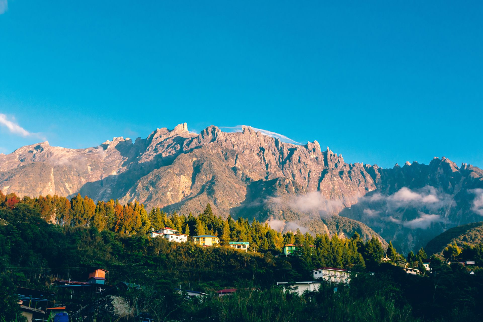 Une vue aérienne à couper le souffle du Mont Kinabalu avec un ciel bleu vibrant et un charmant village en dessous.