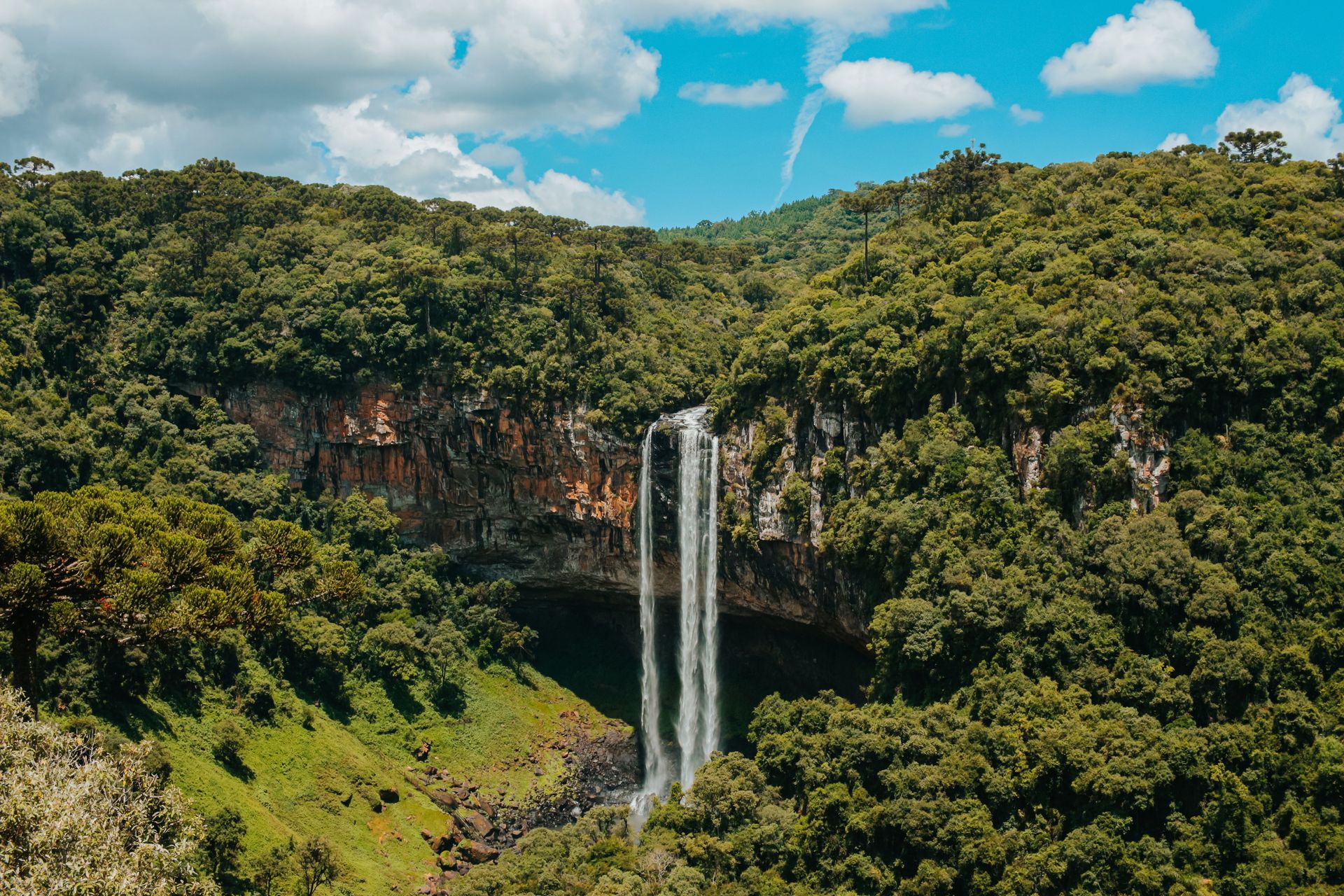 Une vue aérienne époustouflante d'une cascade se déversant à travers une forêt verdoyante sous un ciel bleu éclatant.