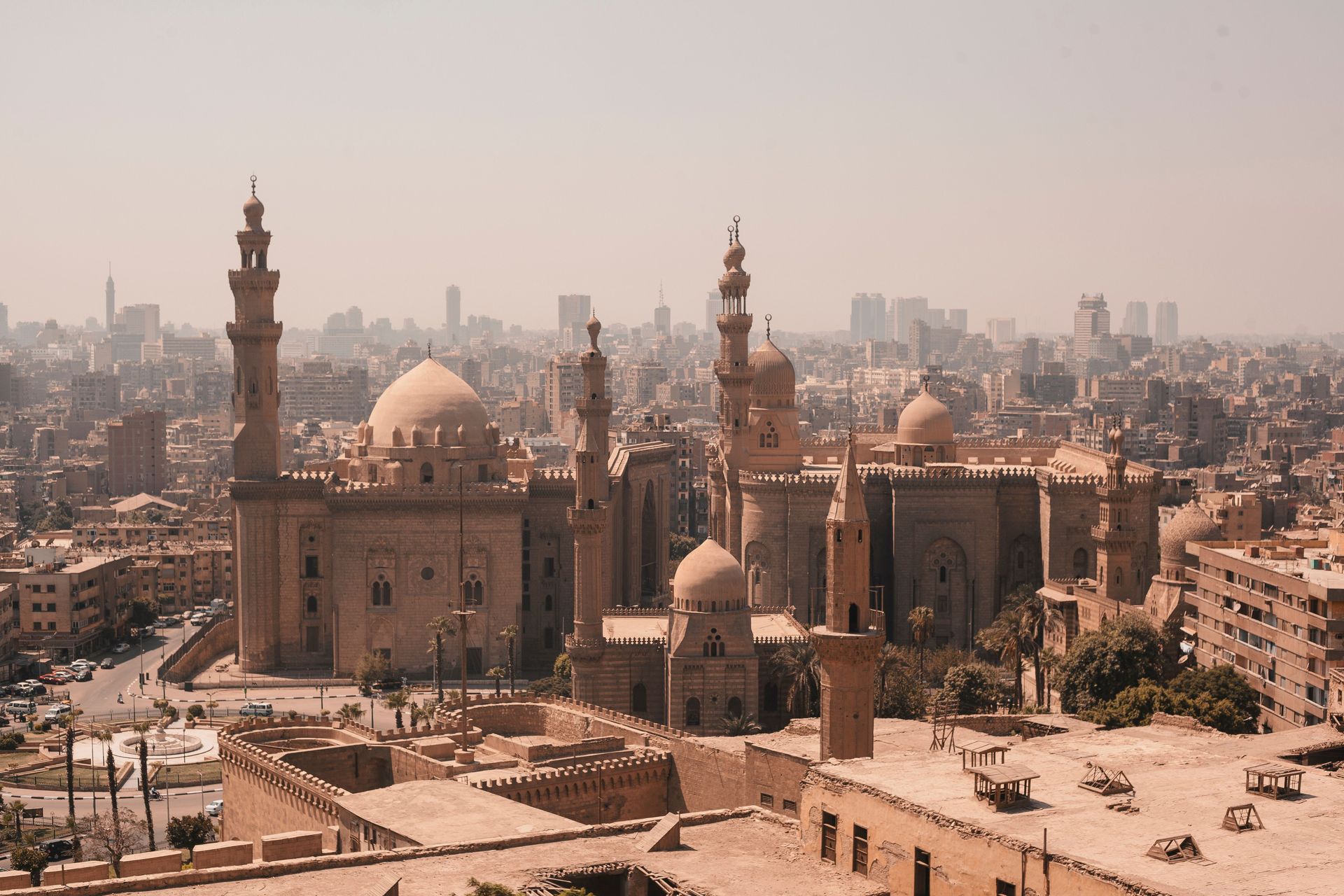 Vue aérienne des mosquées historiques du Caire avec une toile de fond de skyline moderne sous un ciel dégagé.