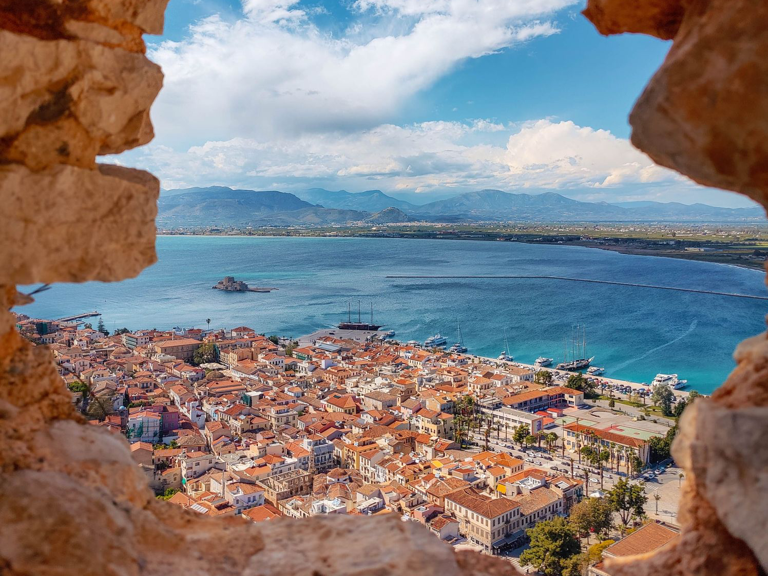 Une magnifique ville côtière vue à travers une ruine en pierre historique, surplombant la mer bleue sereine.