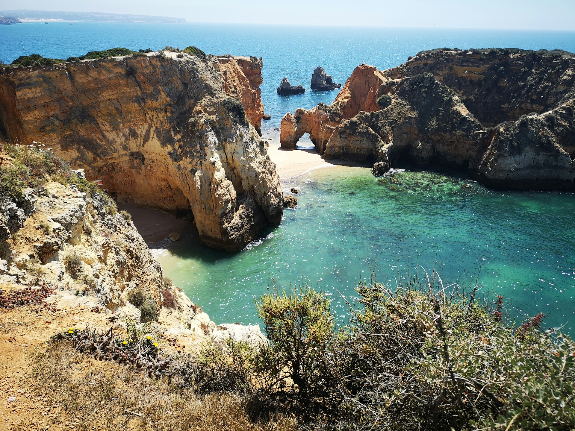 Crique cachée entre falaises ocre de l'Algarve, eau turquoise et arche rocheuse en arrière-plan, à Ponta da Piedade.