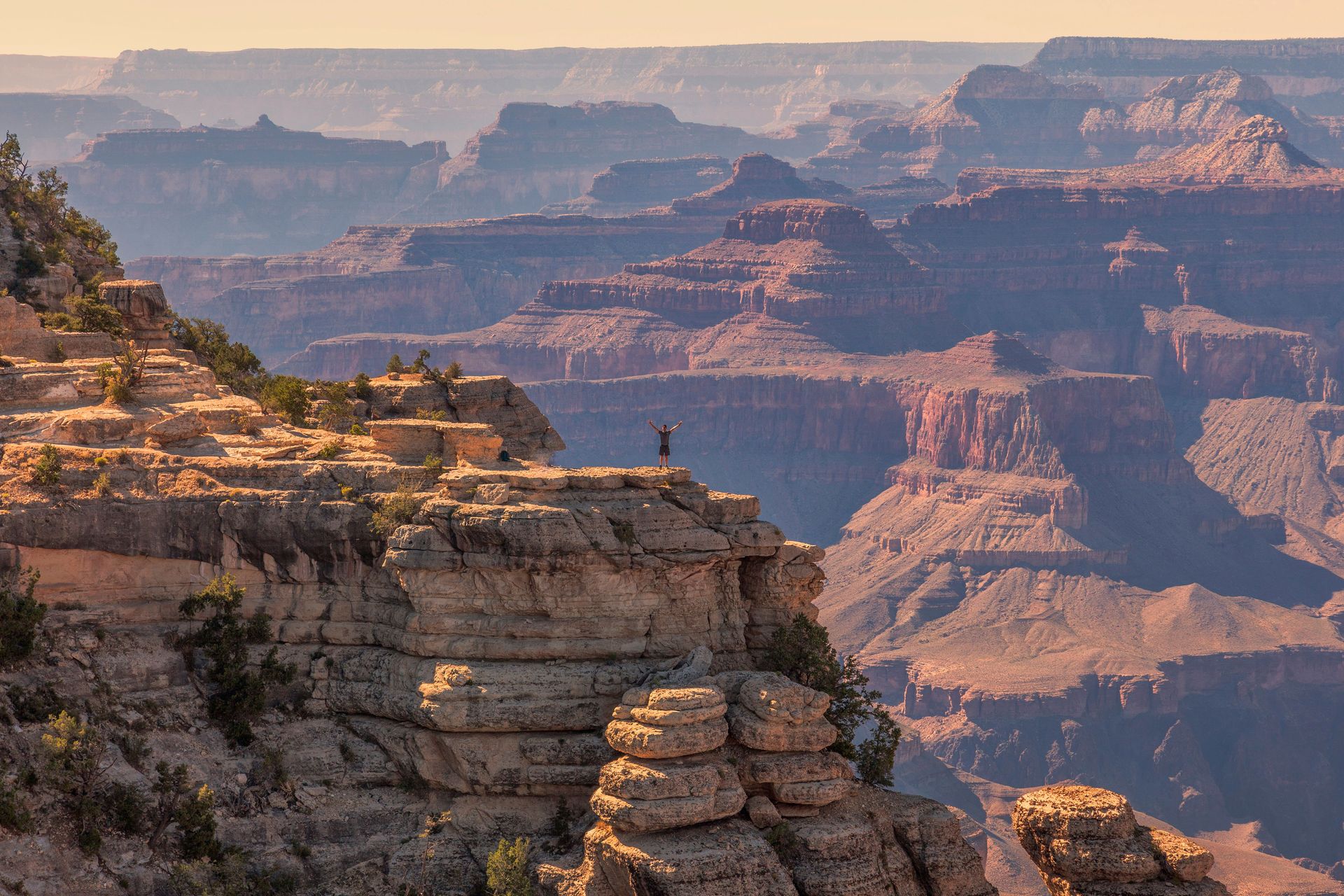 Vue imprenable sur le Grand Canyon, avec une personne debout sur une falaise au coucher du soleil.