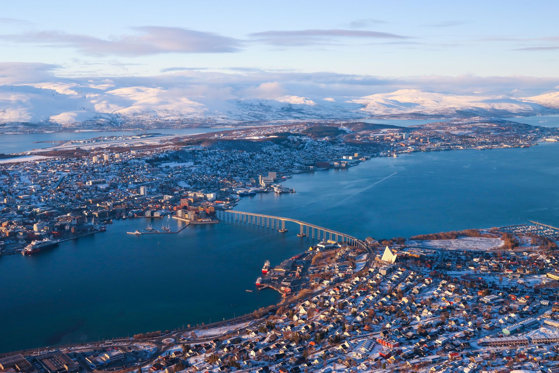 Vue panoramique aérienne de Tromsø, en Norvège, présentant des montagnes enneigées et la cathédrale arctique emblématique.