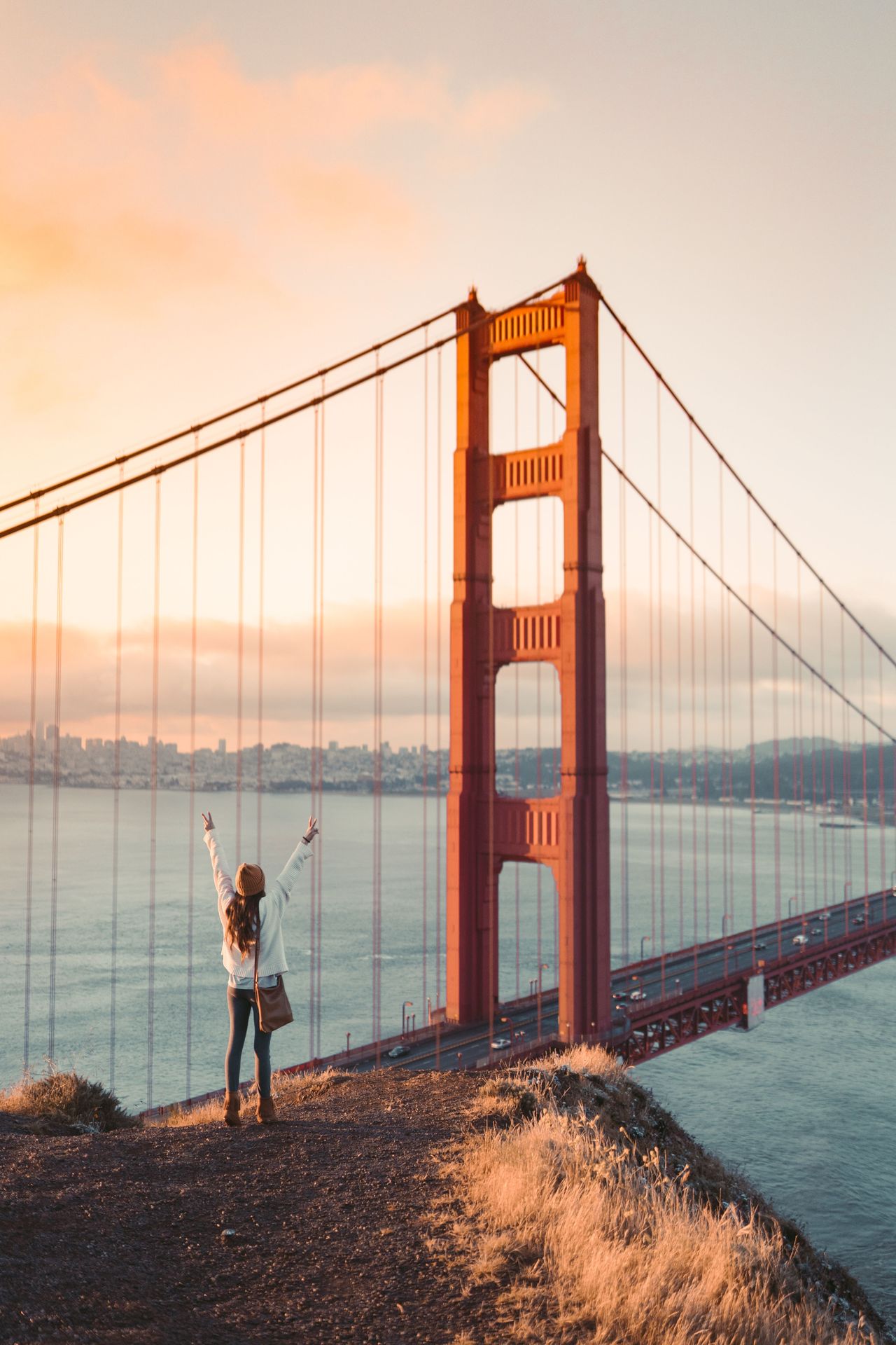Une femme lève les bras de joie près du Pont du Golden Gate à San Francisco au coucher du soleil.
