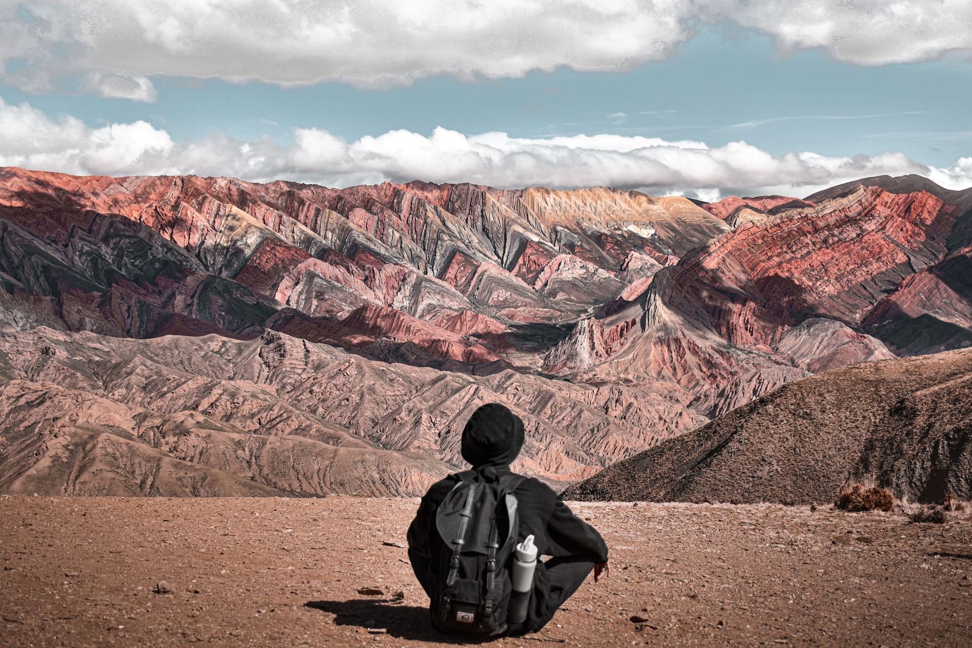 Une personne assise avec un sac à dos apprécie la vue des montagnes colorées de la Serranía de Hornocal à Jujuy, Argentine.