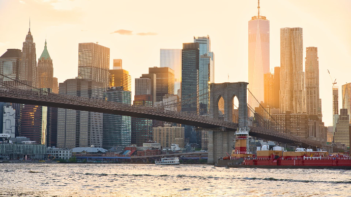 panorama de la ville de New York. Le soleil se couche. Premier plan est un fleuve et second plan le panorama de la ville